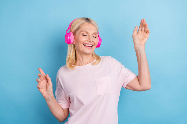 Portret van mooie vreedzame oude dame gesloten ogen tand glimlach dans luister muziek koptelefoon geïsoleerd op blauwe kleur achtergrond. - Foto, afbeelding