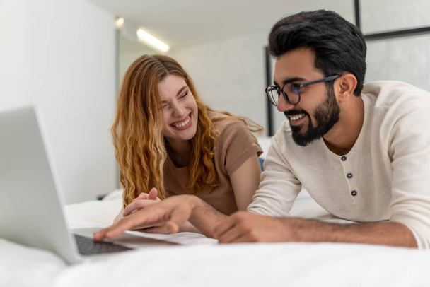 Young happy couple enjoy leisure time at home using laptop computer laying on bed surfing internet together smiling with love. - Φωτογραφία, εικόνα