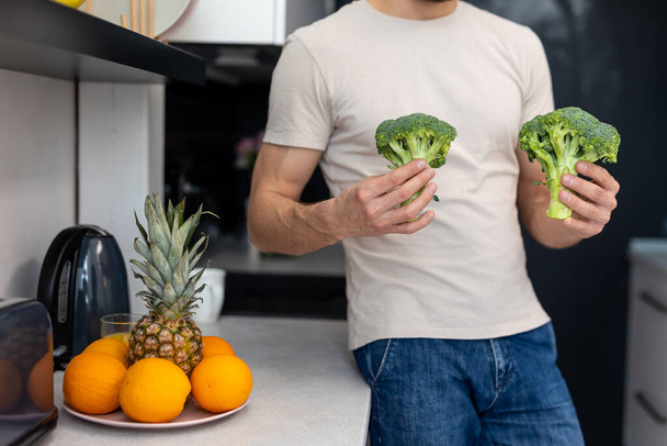 Unknown man holding green fresh broccoli standing in modern kitchen at home. - Фото, изображение