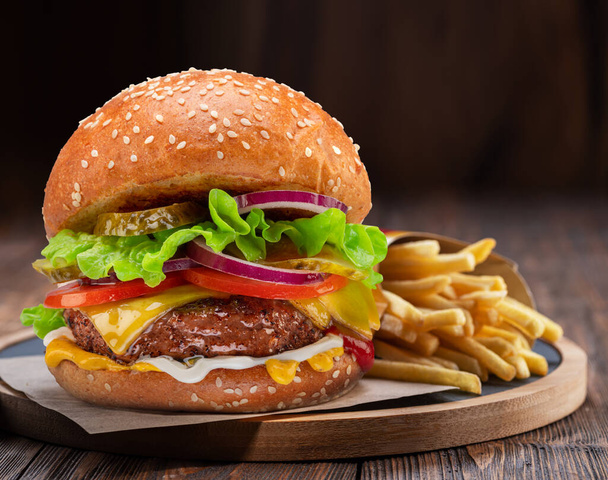 Tasty cheeseburger or hamburger and french fries on wooden tray close-up. - Foto, imagen