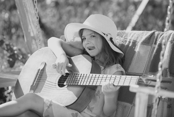 Little girl musician playing guitar. Happy cute teen girl swinging and having fun healthy summer vacation activity. Kids music and songs - Fotografie, Obrázek