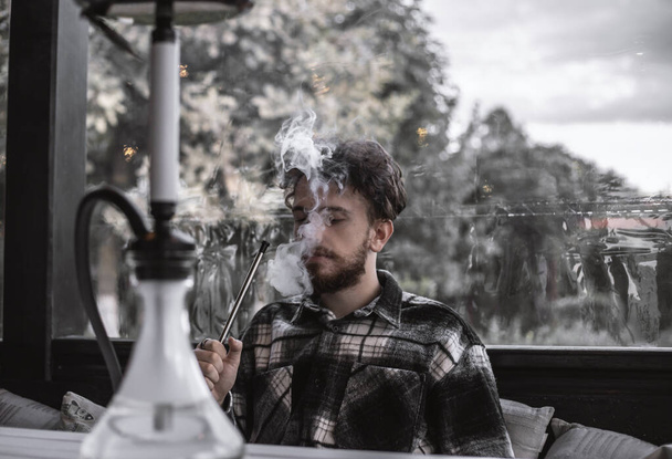 Young handsome boy smoking shisha. Surrounded with smoke. - Photo, image
