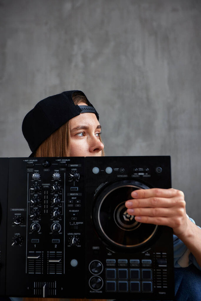 Close-up portrait of a young hip-hop girl in a black baseball cap with a visor back holding a dj mixing console. Musical creativity - Photo, Image