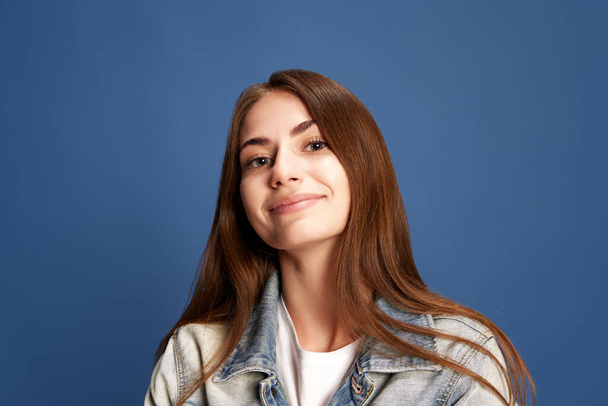 Light smile. Portrait of charming girl, woman with expressive big eyes wearing casual clothes smiling over blue studio background. Concept of happiness, human emotions, fashion, beauty, youth, ad - Photo, Image