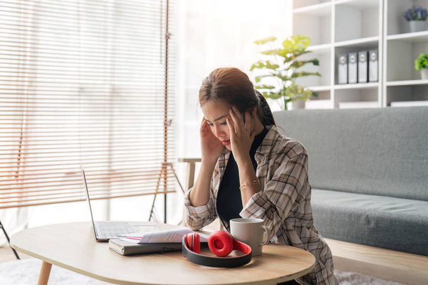 Femme d'affaires fatiguée dans le stress travaille à un ordinateur portable alors qu'elle est assise à une table à la maison et tient sa main sur ses tempes, attaque de migraine. Freelance, travail à domicile. - Photo, image