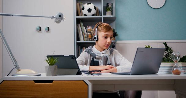 Little cute boy in headphones having a video call talking using laptop sitting in the living room. Online learning, distance learning, learning at home. - Foto, Imagem