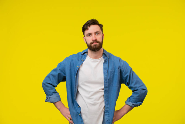 Photo of doubtful unsure man wear turquoise clothes comparing arms empty space isolated yellow color background - Фото, изображение