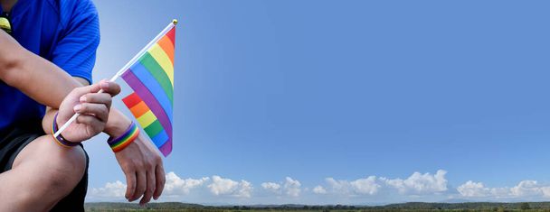 Arcobaleno bandiera alzando sullo sfondo blueskey, spazio copia, concetto per le celebrazioni LGBT nel mese di orgoglio in tutto il mondo. - Foto, immagini