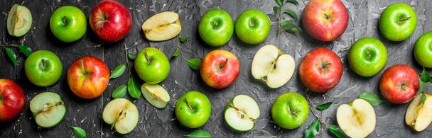 Зеленые и красные сочные яблоки с листьями и яблочными ломтиками. На черном деревенском фоне
. - Фото, изображение