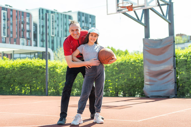 Felice padre e figlia adolescente abbracciando e guardando la fotocamera fuori al campo da basket - Foto, immagini