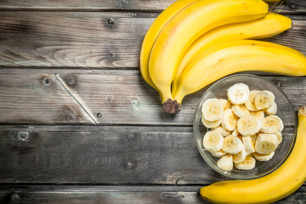 Fresh bananas and banana slices in a glass bowl. On a wooden background. - Foto, immagini