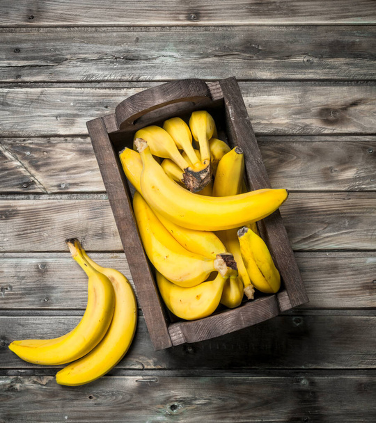 Lots of bananas in a black wooden box. On a black wooden background. - Foto, Imagen