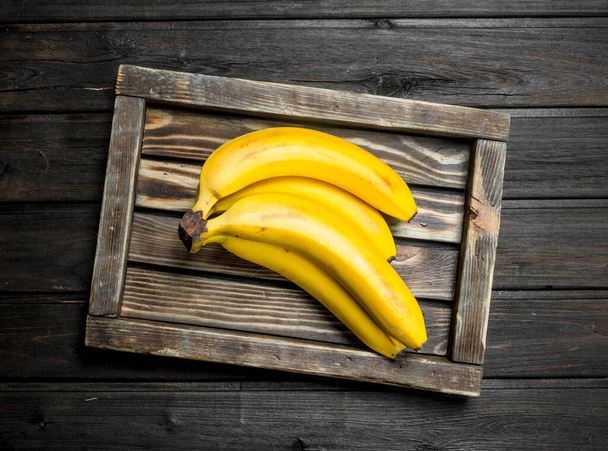 Bunch of bananas in a wooden box. On a black wooden background. - Photo, Image