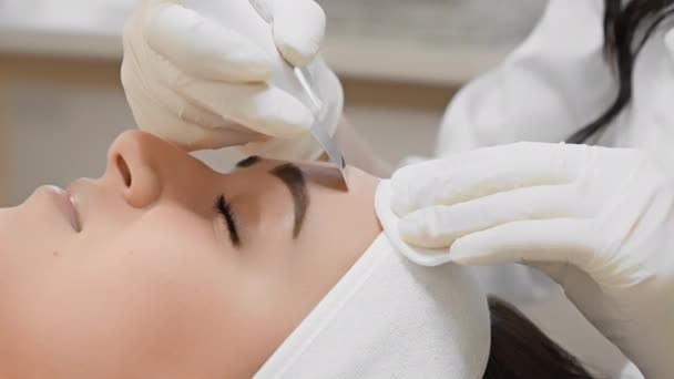 Güzellik salonundaki ultrasonik yüz temizleme dermatolojik terapisi tam bir yüz bakımı sağlar. Güzellik kliniğindeki beyaz eldivenli güzellik uzmanının kozmetik ameliyatındaki bir kadının yakın çekimi. - Video, Çekim
