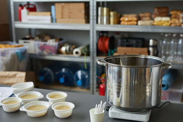 Background image of large saucepan with bowls on table in soup kitchen or help center for refugees, copy space - Photo, Image