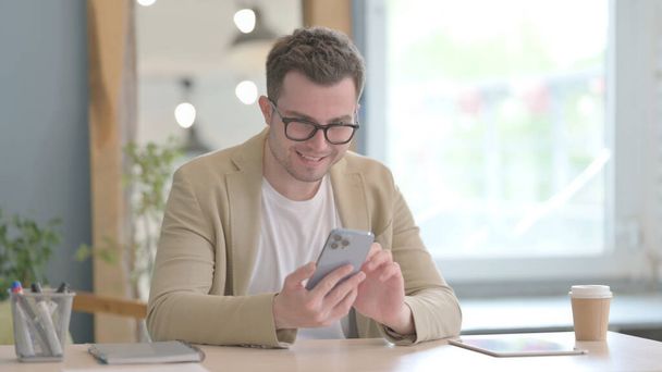 Young Businessman Celebrating Success on Smartphone - Foto, afbeelding