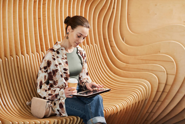 Retrato gráfico de un joven profesional que usa tableta mientras trabaja en un espacio de oficina moderno con sillas de diseño, espacio para copiar - Foto, imagen