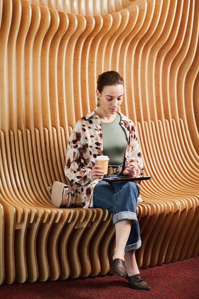 Вертикальний портрет молодого професіонала, який використовує планшет під час роботи на сучасному офісному просторі з дизайнерськими стільцями
 - Фото, зображення