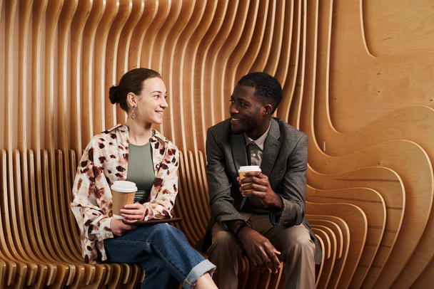 Портрет молодих співробітників, які спілкуються під час відпочинку в лаунжі в сучасному офісному просторі з дерев'яною панеллю
 - Фото, зображення