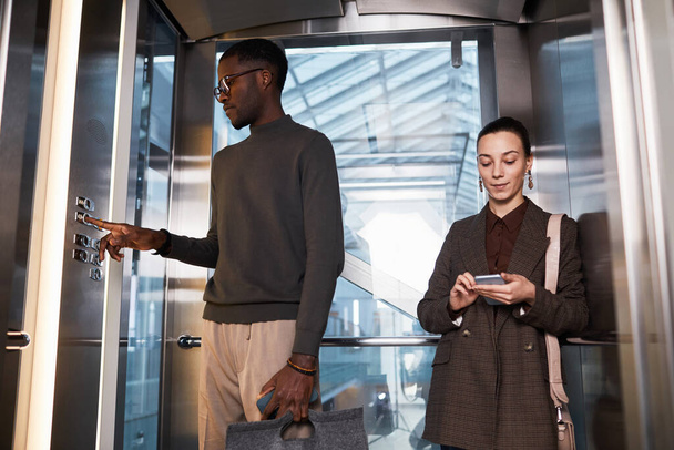Front view of two young business people in glass elevator at modern office building, copy space - Foto, Bild