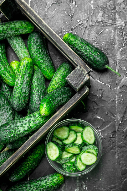 Cucumbers in the box and cucumber slices in the bowl. On rustic background - Foto, imagen