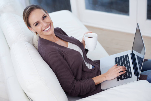 Modern domestic life. A young woman sitting in front of her laptop holding a mug of coffee - Foto, afbeelding