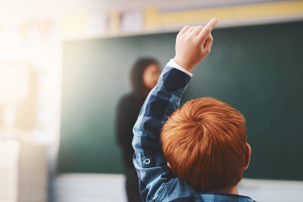 Hand, student and child in classroom with question for teacher, education and learning with school blackboard. Boy, raise arm and questions for knowledge, information and development in class. - 写真・画像