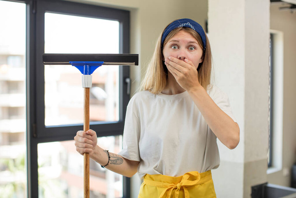 young pretty woman covering mouth with a hand and shocked or surprised expression. windows washer concept - 写真・画像