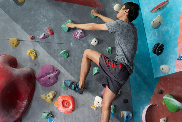 Homme escalade sur mur d'entraînement dans la salle de gym, mâle sportif actif pratiquant l'escalade sur rocher artificiel dans le sport extrême, bloc, mur d'escalade, grimpeur s'entraîne, escalade dans la ville, forte - Photo, image