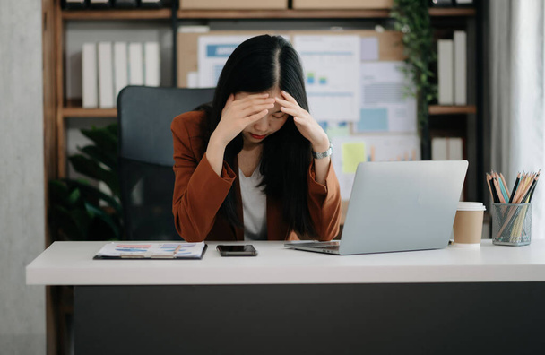 Asian woman feeling migraine head strain.Overworked businesswoman financier with on laptop at modern office. - Foto, immagini