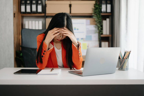 Asian woman feeling migraine head strain.Overworked businesswoman financier with on laptop at modern office. - Foto, immagini