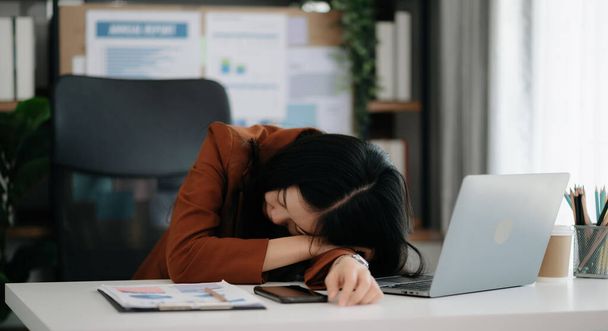 Asian woman feeling migraine head strain.Overworked businesswoman financier with on laptop at modern office. - Fotó, kép