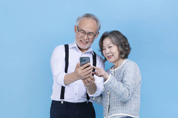 active young senior Korean Asian couple looking at smartphone against studio background - Foto, imagen
