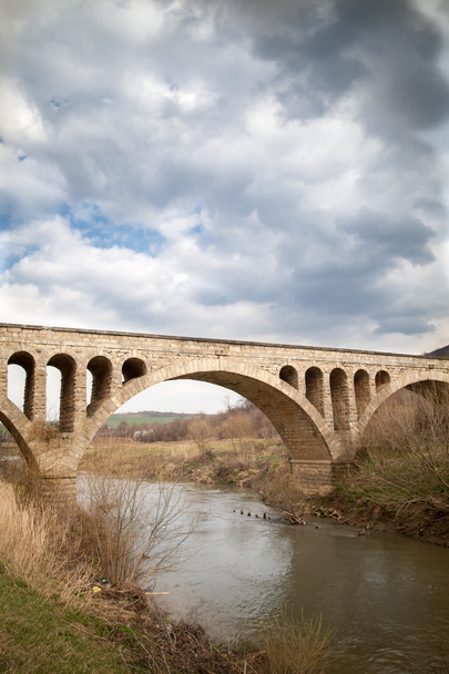 Ponte velha da meia-idade da pedra em Bulgária, de encontro a um céu cloudy
 - Foto, Imagem