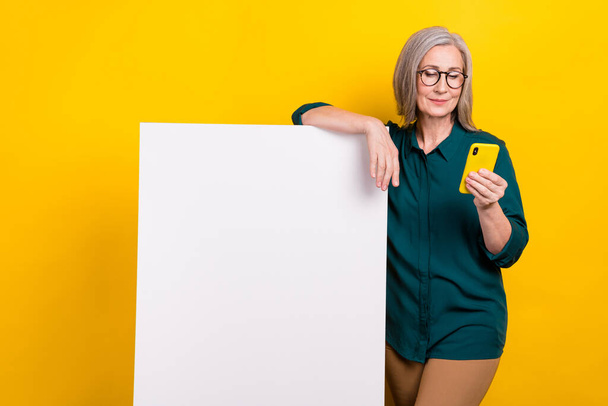 Photo of promoter aged lady search cell gadget enjoying promotion empty card paper wall isolated on bright color background. - Foto, immagini