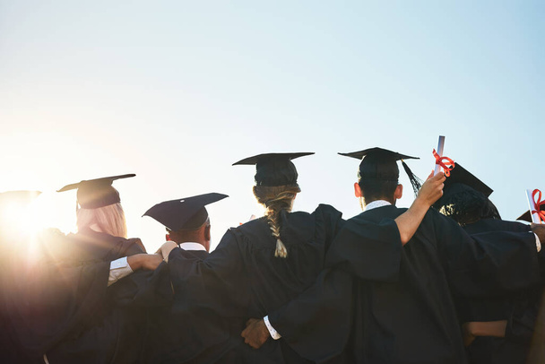 Group, students and graduation for college or university friends together with blue sky mockup. Men and women outdoor to celebrate education achievement, success and future at event for graduates. - 写真・画像