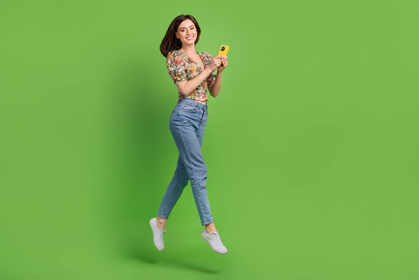 Full length portrait of charming energetic person jumping use smart phone empty space isolated on green color background. - Foto, Bild