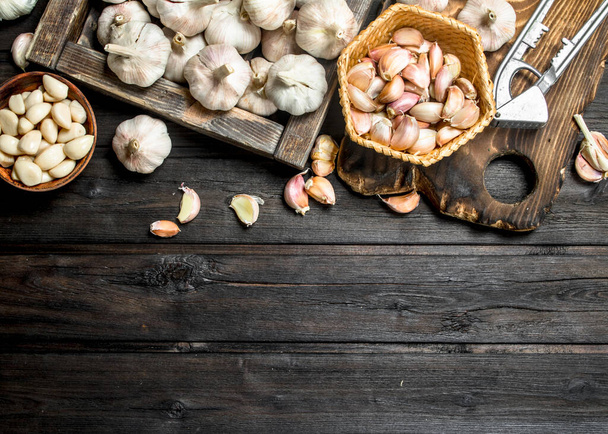 Garlic on a cutting Board with a garlic press. On black wooden background - Foto, afbeelding