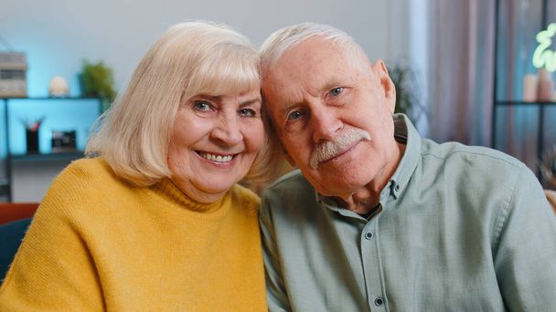Boldog idős, idős család pár ölelkezik, nevet, mosolyog a kamerába, egészséges nyugdíjas két nagyszülő férj felesége. Nagymama nagypapa ölelés ül kanapén otthon, portré - Fotó, kép