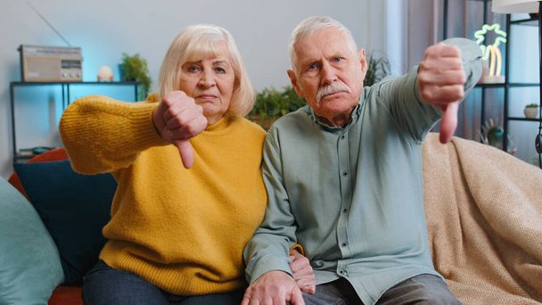 Nem tetszik. Feldúlt családfő nagyszülők férfi nő mutatja hüvelykujját lefelé jel, kifejezi elégedetlenség, rosszallás, elégedetlen rossz munka otthon. Elégedetlen öreg nagymama, nagyapa pár kanapén - Fotó, kép
