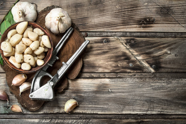 Cloves of fresh garlic on a cutting Board with a garlic press. On wooden background - Foto, Imagen