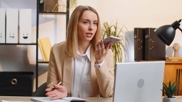 Blonde businesswoman working, having mobile phone loudspeaker talk at office desk with laptop. Manager freelance young woman holding smartphone using messenger chat apps. Employment, occupation - Photo, Image