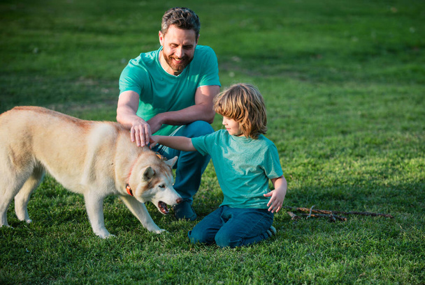 Father and son playing with dog in the garden. Dad and child with pet having fun outdoors - Photo, Image