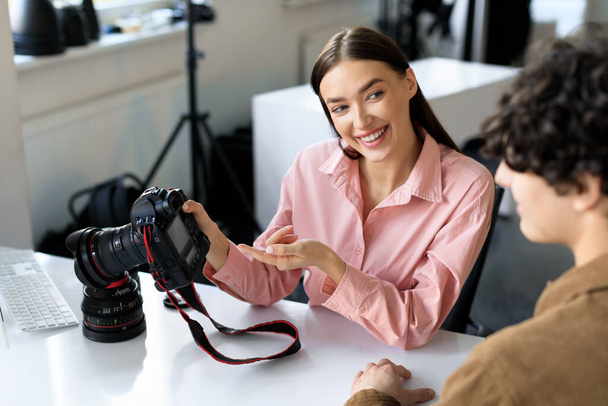 Moments captured. Young photographer woman showing photos work to male model in studio, talking after photoshoot and choosing the best pictures, sitting at workplace - Foto, afbeelding