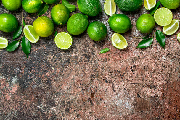 Pieces of ripe lime and a whole fresh lime. On rustic background - Foto, imagen