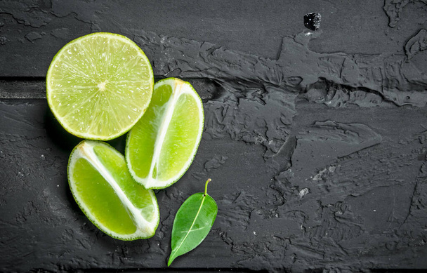 Slices of fresh juicy lime. On black rustic background - Zdjęcie, obraz