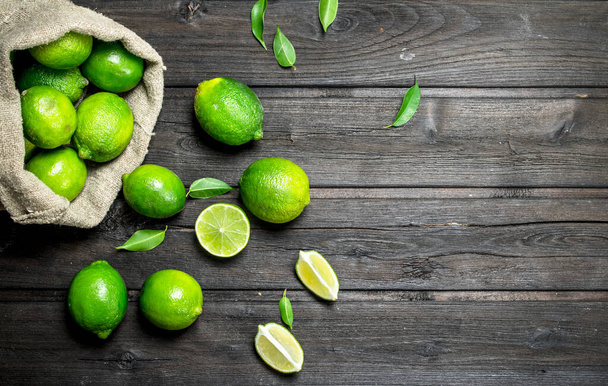 Fresh lime in the sack and pieces of juicy lime. On wooden background - 写真・画像