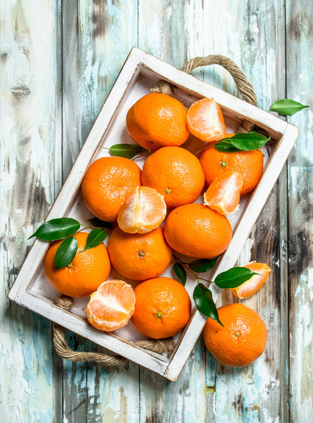 Fresh ripe mandarins with leaves in tray. On wooden background - Fotografie, Obrázek