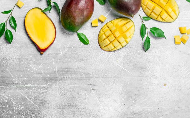 Whole and pieces of ripe mango with leaves. On rustic background - Zdjęcie, obraz