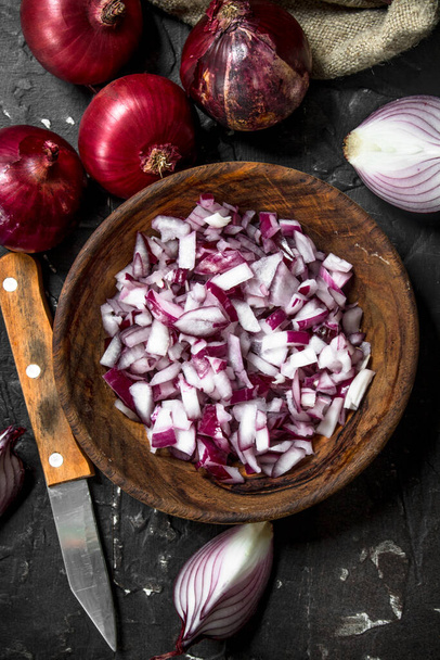Pieces of red onion in bowl with knife. On black rustic background - Foto, imagen